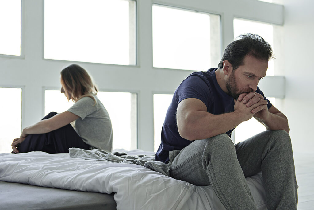 a man and woman sit on a bed after an argument, one of them dealing with anger in recovery
