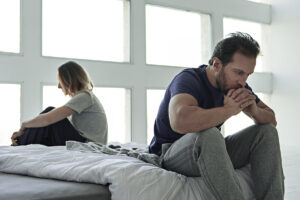 a man and woman sit on a bed after an argument, one of them dealing with anger in recovery