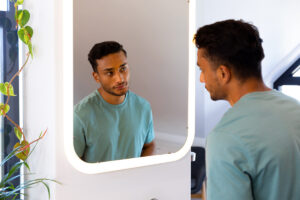 a young man looks in a mirror wondering about men and body image issues