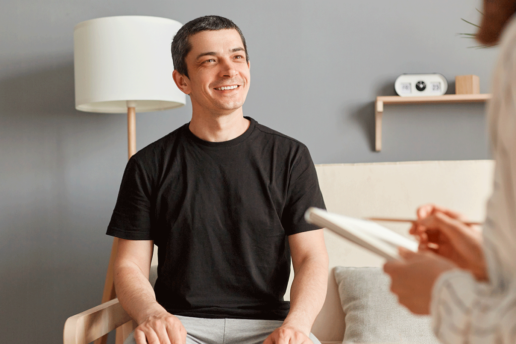 a young man smiles while talking with a therapist about addiction recovery for men