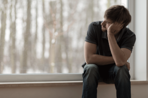 a young man struggling with depression and alcoholism sits sadly on a windowsill