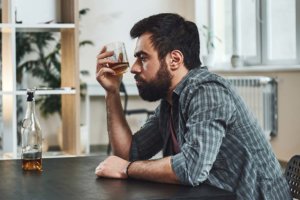 man sitting at table drinking alone showing alcoholism in men