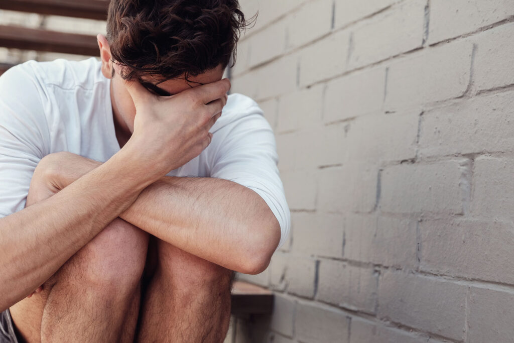 a young man holds his head while struggling with ptsd symptoms in men