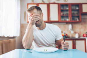 a young man looks ashamed in front of an empty plate, possibly in need of an anorexia treatment program