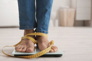 a person's feet on a scale with a tape measure that's fallen to the floor. obsession about body image may be a sign a bulimia treatment program can help