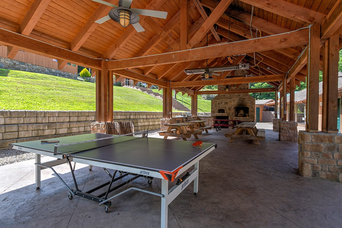 an outdoor covered patio with a large grill and fireplace near picnic tables and a ping pong table