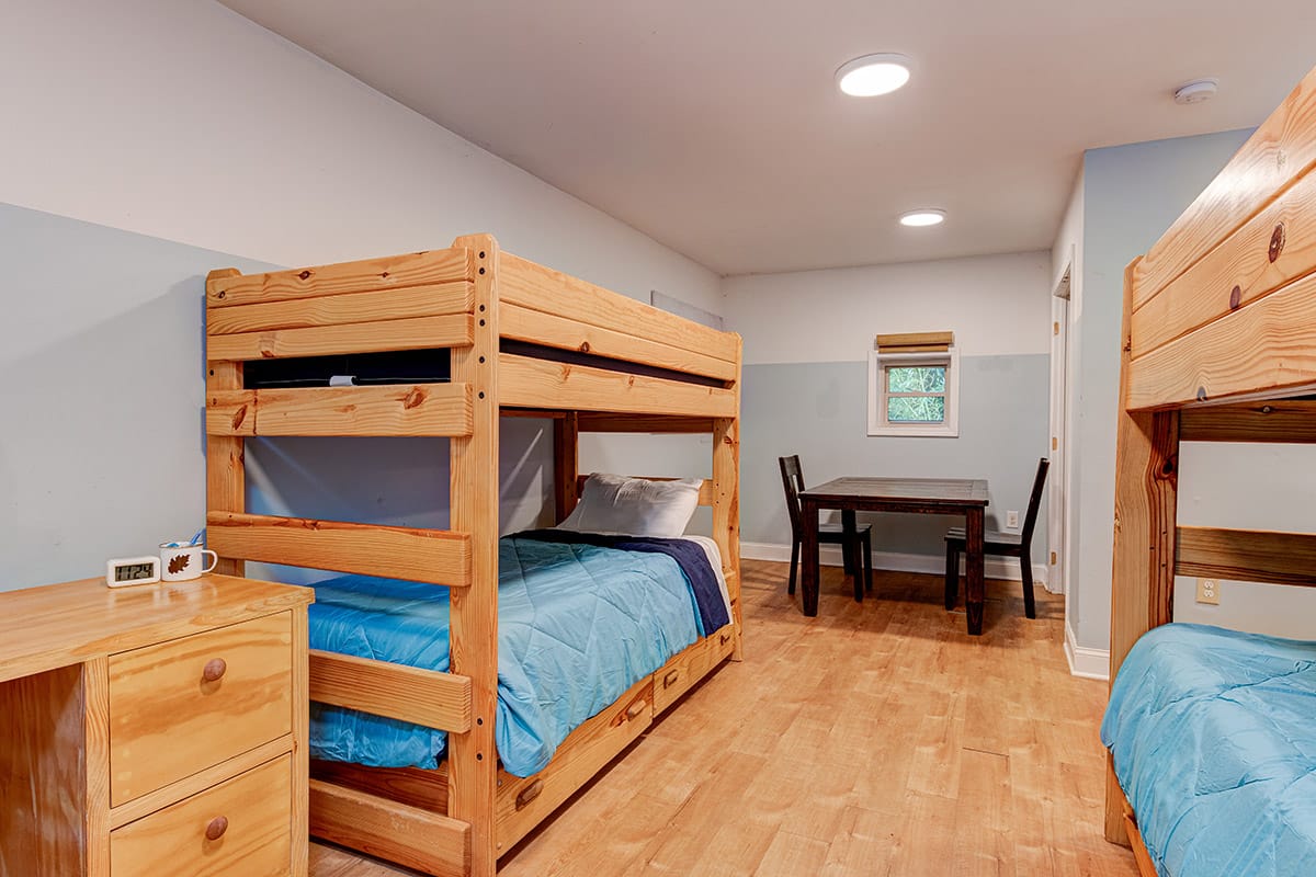 a room with two sets of bunk beds, a desk, a table, and two chairs