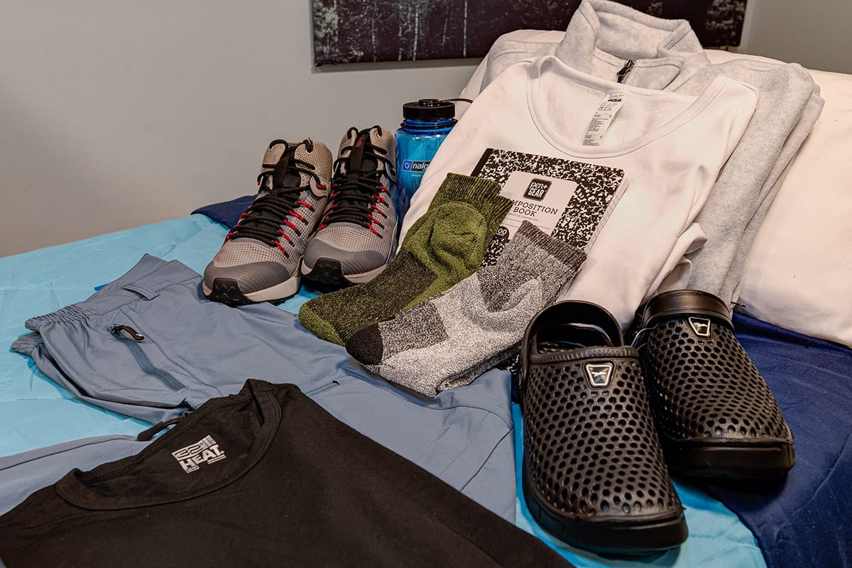 simple clothes, shoes, a water bottle, and notebook on a bed