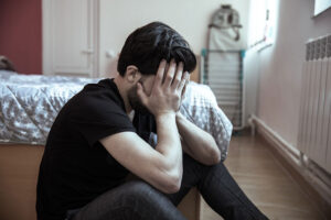 a young man in need of panic disorder treatment sits on a floor with his head in his hands