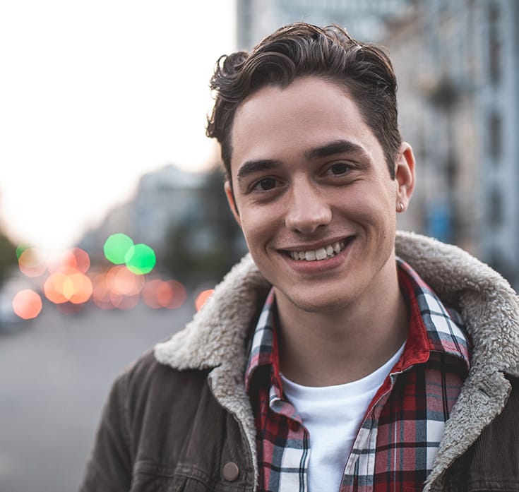 a young man smiles near a busy street
