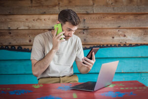 a young man in need of screen addiction treatment consults two smartphones and a laptop