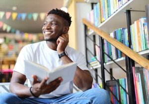 a young man in a library smiles while reading Red Oak Recovery<sup>®</sup> testimonials