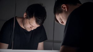 a young man looks sad in a mirror after learning about signs of fentanyl overdose