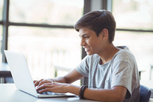 teen boy smiles sitting with a computer on a desk