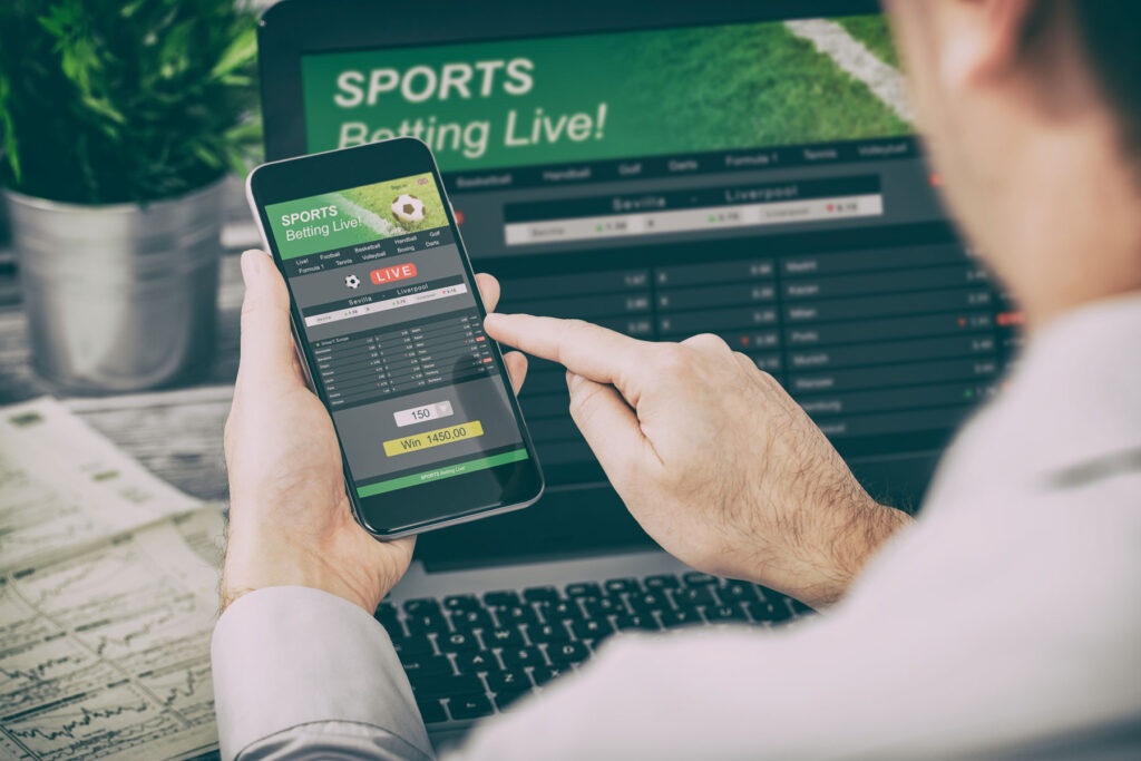a person with sports betting addiction places wagers on a phone and computer