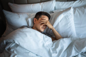 a man lays in bed in pain after self-medicating with alcohol