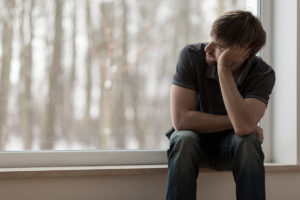 a man looks sad on a windowsill after recognizing the signs of meth use